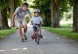 Тато вчить дитину тримати кататися на велосипеді 